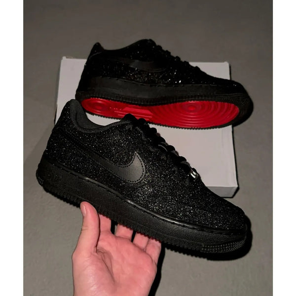 Black glittery sneakers with red soles on a gray surface
